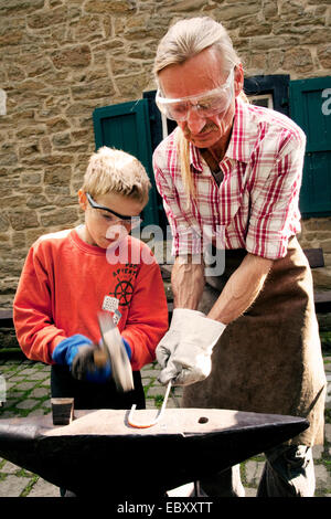 boy forging with blacksmith, Germany, North Rhine-Westphalia, Ruhr Area, Witten Stock Photo