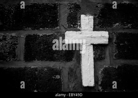 A white stone cross against a black brick wall. Stock Photo