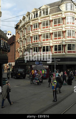 Portrait people crossing Tib Street at Market Street, balloons stall and vendor selling Big Issue in North magazine, Manchester Stock Photo