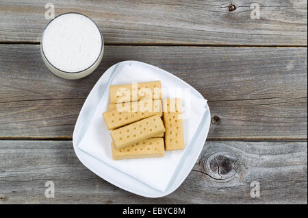 Top view of butter cookies on white cloth napkin and a glass of rich milk with rustic wood underneath Stock Photo