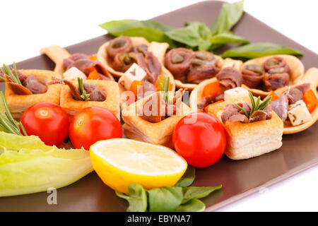 Anchovies in pastries, lemon, tomato, lettuce and basil on brown plate. Stock Photo
