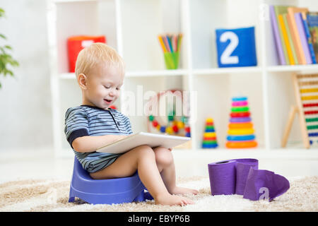smiling kid sitting on chamber pot playing tablet pc Stock Photo