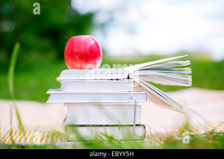 pile of books with one book open and red apple on nature background Stock Photo