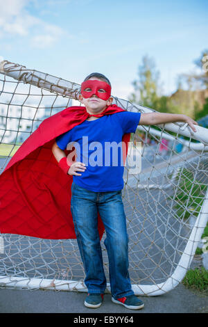 Boy dressed in cape and mask leaning on football goal Stock Photo