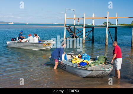 Men & family climbing into dinghies on edge of vast blue waters of ocean inlet, going fishing at Australian holiday destination Stock Photo