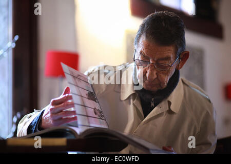Portrait of an Italian senior citizen sitting in a wine bar, being sunk in a book of photography. Spilimbergo, Italy Stock Photo
