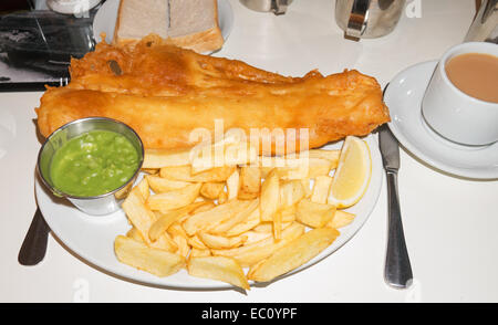 Plate of fish and chips with mushy peas, bread and cup of tea. Stock Photo