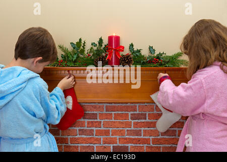 A boy and a girl hanging their stockings over the fireplace on Christmas Eve Stock Photo