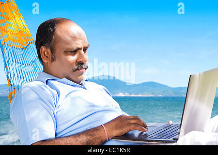 indian man beach working laptop Stock Photo