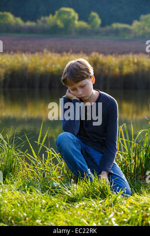 Sad boy sitting on a small lake, Wandersleben, Thuringia, Germany Stock Photo