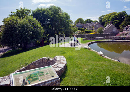 A lady visitor sits by the duck pond in the centre of Worth Matravers Dorset England  UK Stock Photo