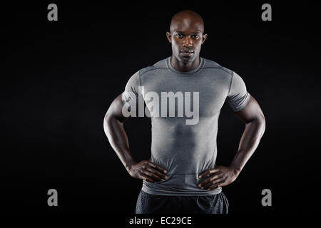 Portrait of muscular young man in sportswear standing with his hands on hips looking at camera against black background. Stock Photo