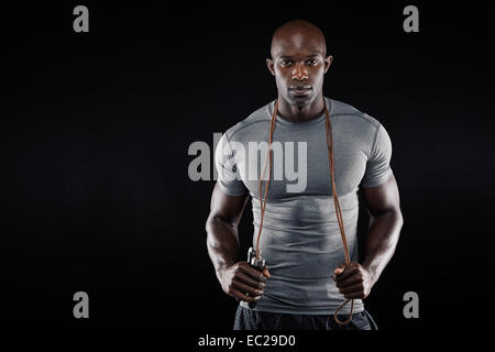 Handsome muscular man posing with jumping rope on black background. African fitness model with skipping rope. Stock Photo