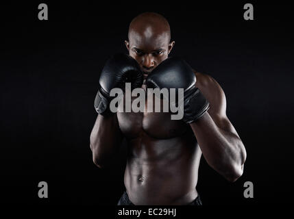 Portrait of tough male boxer posing in boxing stance against black background. Professional fighter ready for boxing match. Stock Photo