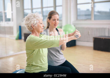 Senior woman being assisted by instructor in lifting dumbbells at gym. Senior woman training in the gym with a personal trainer Stock Photo