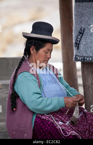 Peruvian woman seated,  knitting at country market stall. Stock Photo