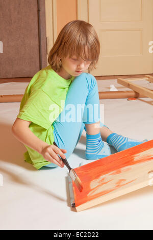 Boy with Blond Hair Painting a Board with Red Color Stock Photo