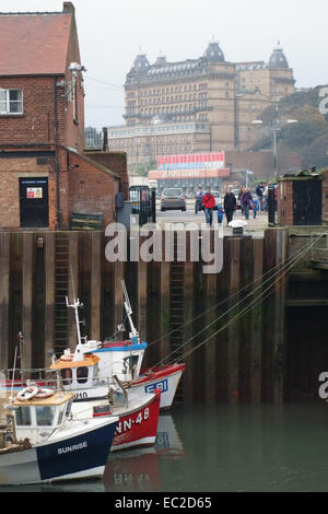 View of the Grand Hotel through buildings surrounding the harbour and fishing boats in Scarborough, North Yorkshire on a grey au Stock Photo