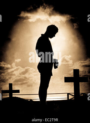 Silhouetted in the golden glory of a Pacific sunrise, crosses mark the graves of American boys who gave their lives to win a small atoll on the road to the Philippines.  A Coast Guardsman stands in silent reverence beside the resting place of a comrade.  1944. Stock Photo