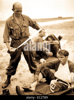 An American medium tank hit a Japanese land mine in surging forward to the Tacloban Air Strip during the early stages of the Philippines invasion.  Here, one of the wounded from the wrecked tank is being bandaged by a medical corpsman. 1944. Stock Photo