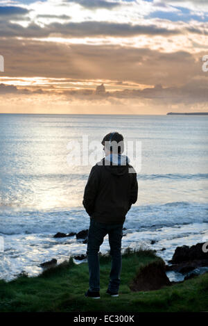 A teenage boy listens to his iPod while looking at the view at Manorbier Bay near Tenby in Pembrokeshire, Wales UK Stock Photo