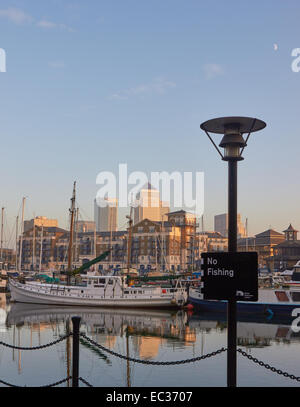 Boats moored in Limehouse Basin at dusk with Canary Wharf in background and daytime moon east London England Europe Stock Photo