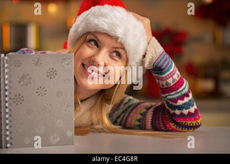 Portrait of thoughtful teenager girl in santa hat with notepad Stock Photo