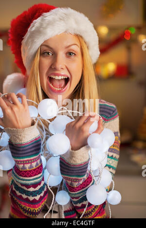 Portrait of happy teenager girl in santa hat holding tangled christmas lights Stock Photo