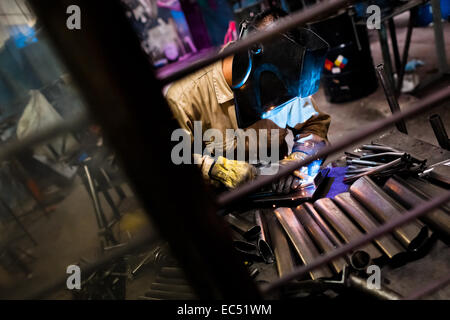 A bicycle welder works on a bike frame fixed on a welding jig in a small scale bicycle factory in Cali, Colombia, 27 June 2014. Due to the strong, vibrant cycling culture in Colombia, with cycling being one of the two most popular sports in the country, dozens of bike workshops and artisanal, often family-run bicycle factories were always spread out through the Colombian cities. However, growing import of cheap bicycles and components from China during the last decade has led to a significant decline in domestic bicycle production. Traditional no-name bike manufacturers are forced to close dow Stock Photo