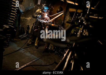 A bicycle welder works on a bike frame fixed on a welding jig in a small scale bicycle factory in Bogota, Colombia, 10 April 2013. Due to the strong, vibrant cycling culture in Colombia, with cycling being one of the two most popular sports in the country, dozens of bike workshops and artisanal, often family-run bicycle factories were always spread out through the Colombian cities. However, growing import of cheap bicycles and components from China during the last decade has led to a significant decline in domestic bicycle production. Traditional no-name bike manufacturers are forced to close Stock Photo
