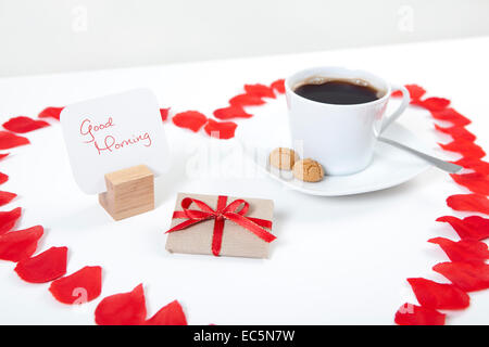 breakfast table for Valentine's Day with gift and coffee framed with a heart made of rose petals Stock Photo