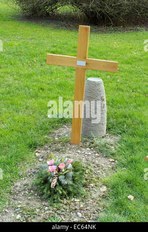Simple wood cross and flower on a cemetery tomb in green grass Stock Photo