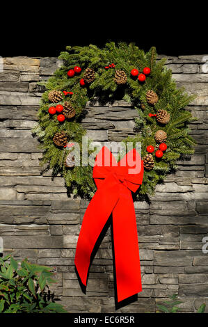 Christmas wreath with pine cones and large red bow hanging on a natural stone wall