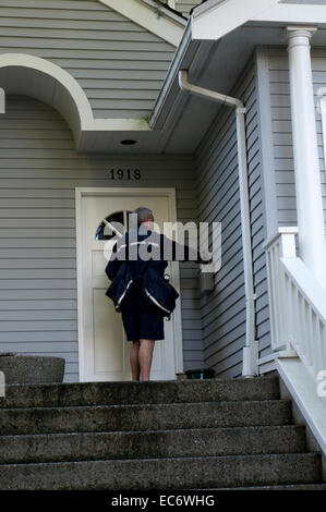 Canada post letter carrier placing mail in a residential mailbox, Vancouver, BC, Canada Stock Photo