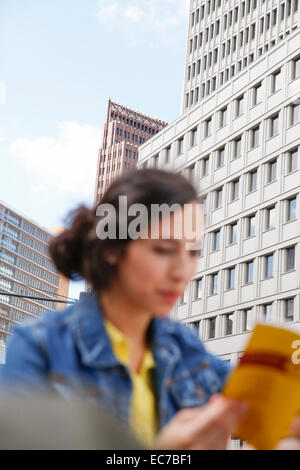 Germany, Berlin, young woman reading guidebook in front of facades at Potsdam Square Stock Photo
