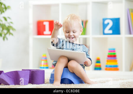 smiling kid sitting on chamber pot with toilet paper rolls Stock Photo