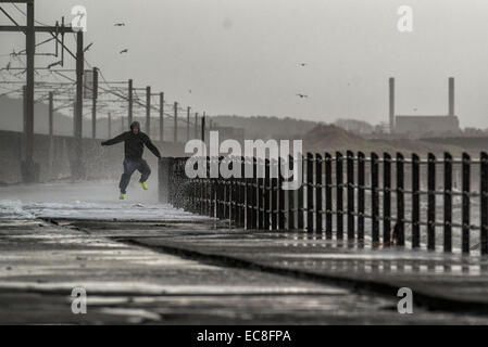 A man jumps the waves as they crash over the promenade wall on December 10, 2014 in Saltcoats, Scotland. Stock Photo