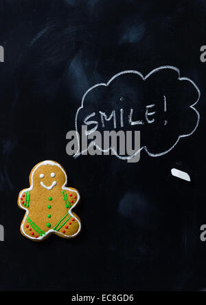 The gingerbread man says "Smile" over black chalkboard, above view Stock Photo