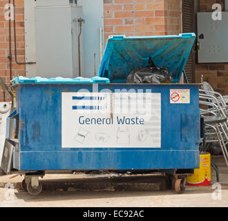 Large blue skip / waste disposal bin with lid raised & plastic bags of rubbish visible at rear of shops in city centre Stock Photo