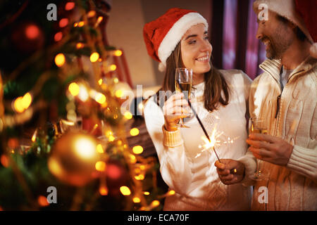 Cheerful couple with champagne and Bengal light celebrating Christmas at home Stock Photo