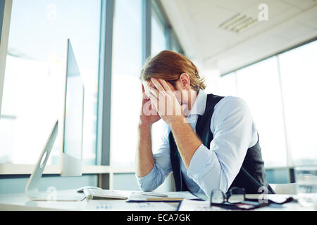Tired businessman touching his head while looking at monitor in office Stock Photo