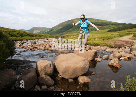 Woman crossing River Brittle on stepping stones, Glen Brittle, Isle of Skye, Scotland, United Kingdom Stock Photo