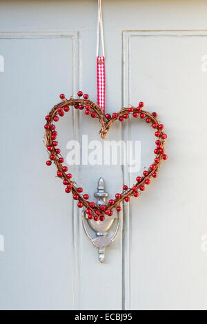 Red berry heart christmas wreath hanging on a wooden door Stock Photo