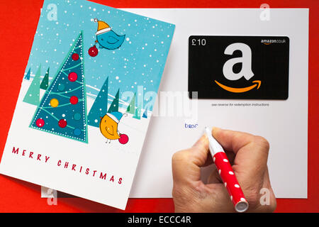 writing in an Amazon Merry Christmas giftcard with birds decorating christmas tree gift card set on red background Stock Photo