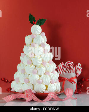 Christmas tree dessert treat made with pink and white meringues with candy cane decorations against a red background. Stock Photo