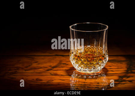 Liquor in a diamond-cut tumbler on a textured wooden table.  Spot light for focus. Upper frame fades to black. Stock Photo