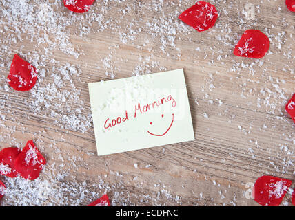 A wooden background with snowflakes and  roses flowers. in the middle a note with the text good morning Stock Photo