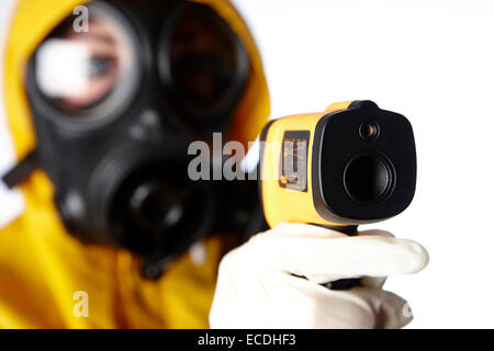 woman wearing protective clothing and gas mask face protection using infra red thermometer to check for flu virus fever symptoms in a pandemic concept Stock Photo
