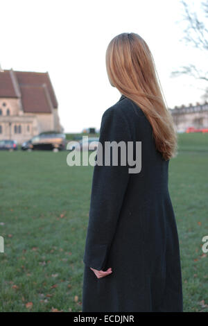 Rear view shot of a young woman standing looking into the distance in a park and a corner of a church. Stock Photo