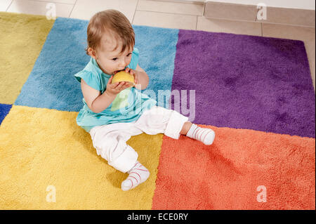 Baby girl 1 year old eating orange carpet Stock Photo